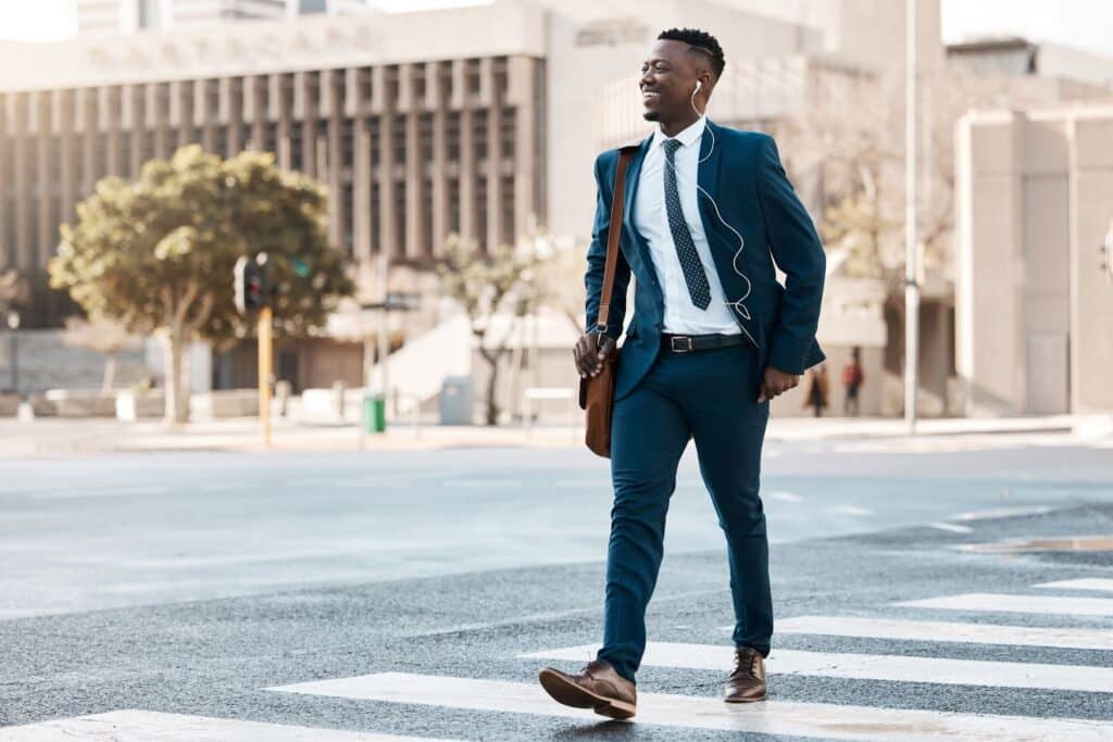 A PT owner wearing a professional navy blue suit and a patterned tie smiles as he walks across a city crosswalk.