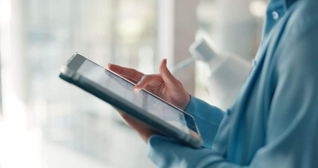 A person wearing a blue shirt uses a finger to navigate on a tablet held in their hands.