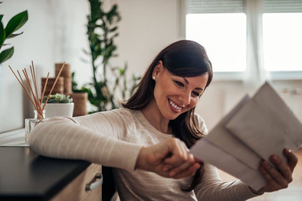 A smiling woman with long brown hair is sitting indoors, reading the PT newsletter.