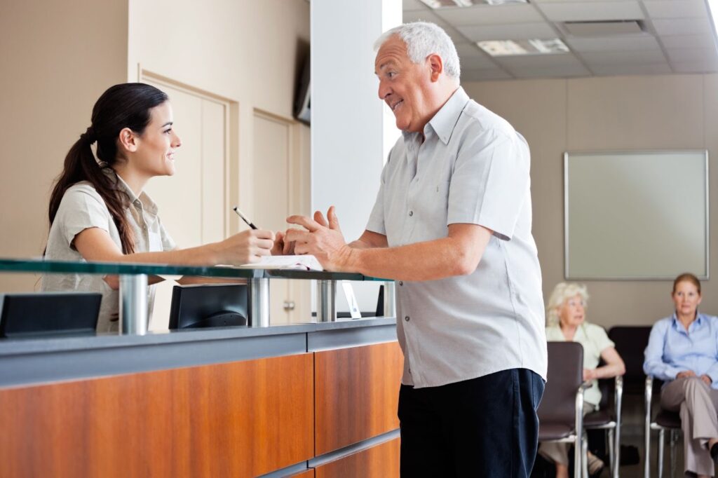 In a clinical setting, a male patient is talking to a female receptionist.