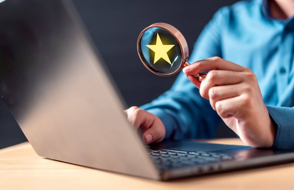A person using a magnifying glass with a yellow star graphic to search or evaluate information on a laptop.