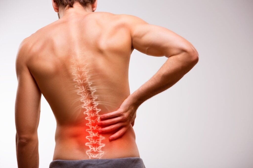 A rear view of a shirtless man holding his lower back in pain, with a glowing red anatomical illustration of the spine overlaid on his back.