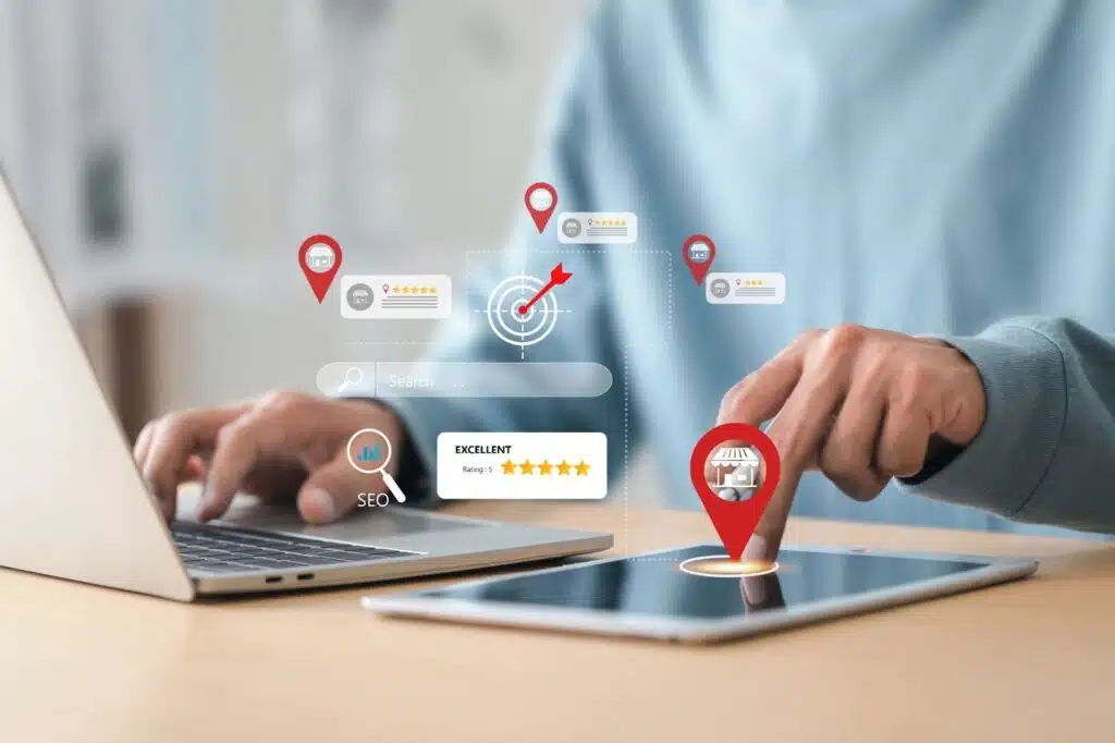 A person using a laptop and tablet with digital overlays representing local SEO and business marketing, including red map pins, a target icon, star ratings, and a search bar.