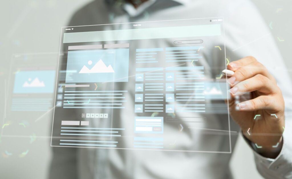 A person's hand using a stylus to interact with a transparent, glowing digital interface that displays a website wireframe or layout with image placeholders and text sections.