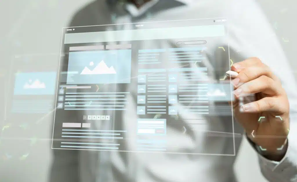 A person's hand using a stylus to interact with a transparent, glowing digital interface that displays a website wireframe or layout with image placeholders and text sections.